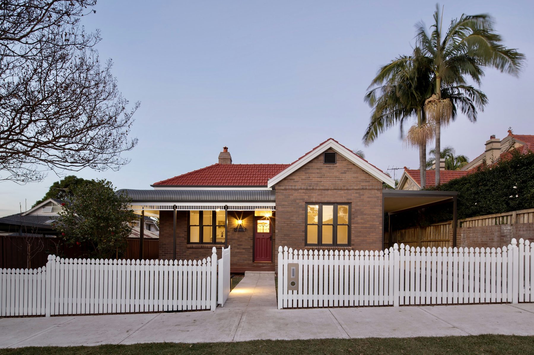 Restored character brick bungalow with white picket fence at dusk